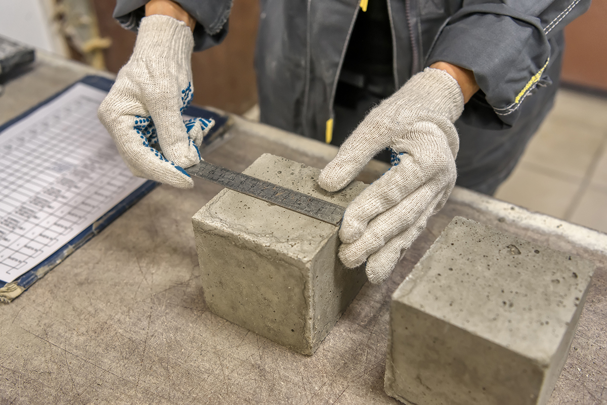 Laboratory for testing building materials. Lab technician measures the size of a concrete cube using a metal ruler.